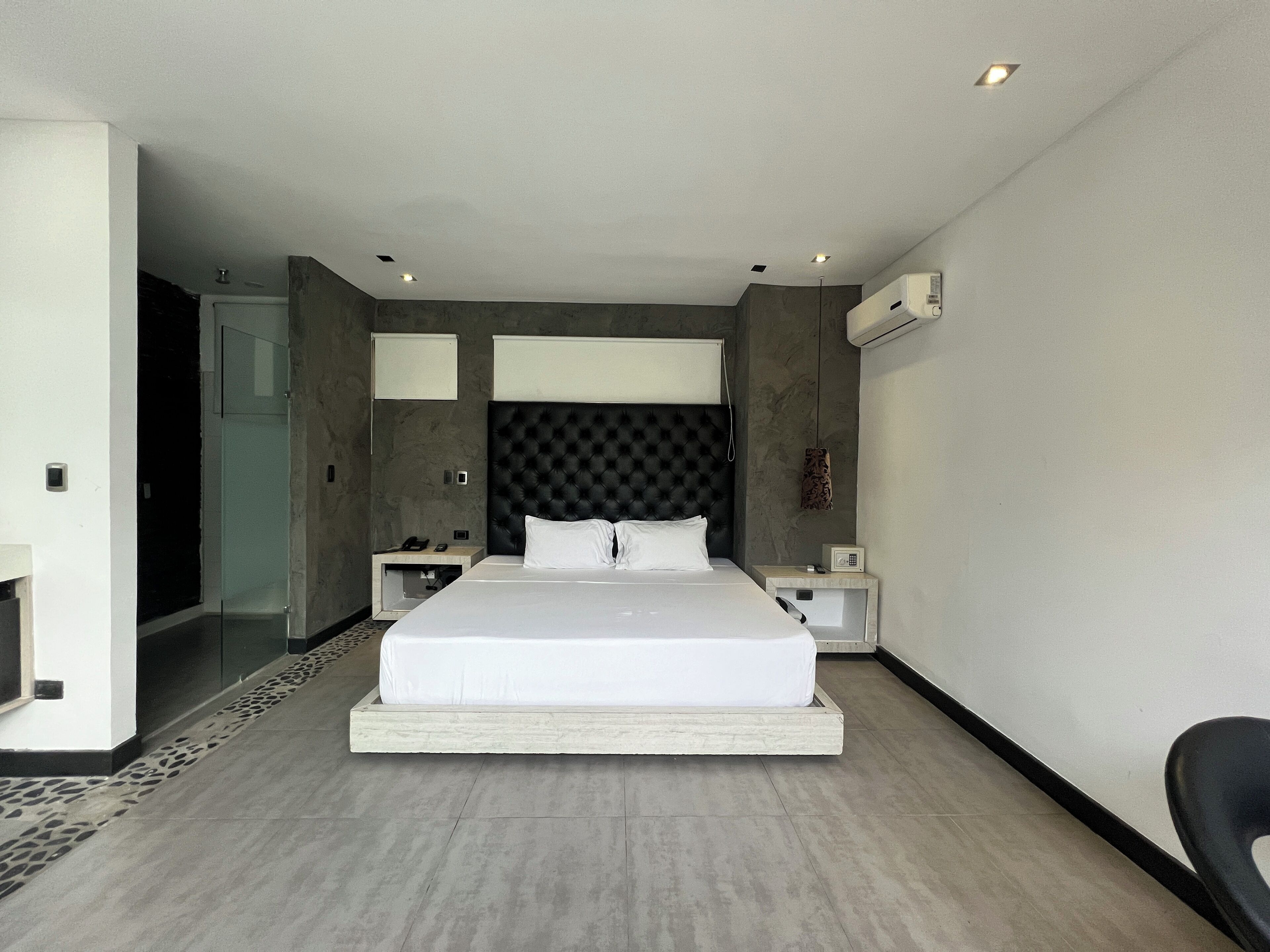 A modern hotel room with a large bed, bedside tables, a built-in wardrobe, and an air conditioning unit.