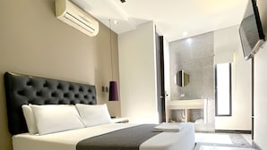 A modern bedroom with a large bed, an air conditioning unit, a TV, and a bathroom visible through an open door. - Hotel 47 Medellin Street (Medellín)