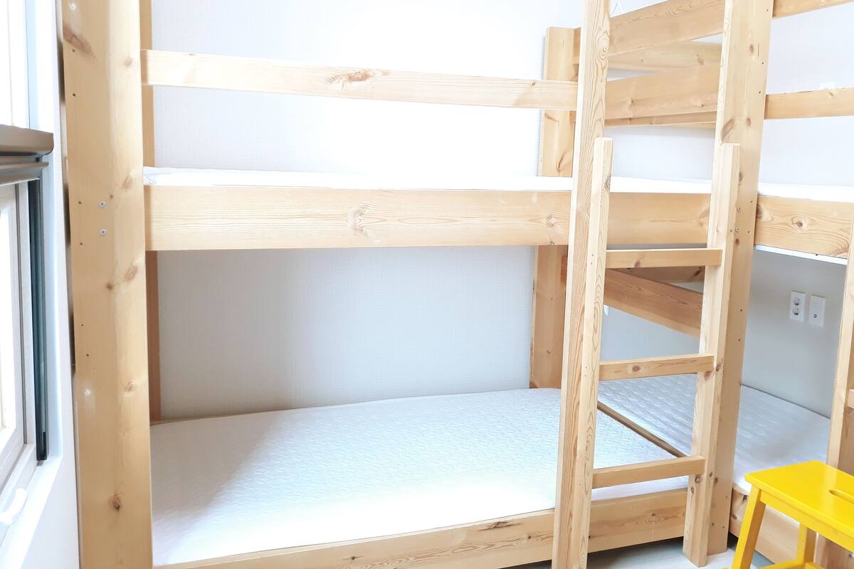 A bunk bed with a ladder, a window, and a yellow chair.