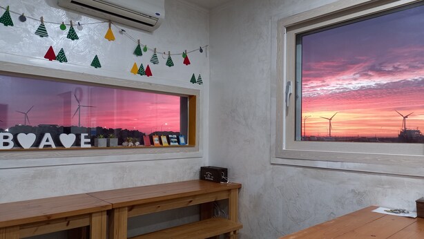 Una habitación con una mesa de madera, un banco, una ventana que ofrece vistas al atardecer y un aire acondicionado instalado en la pared.