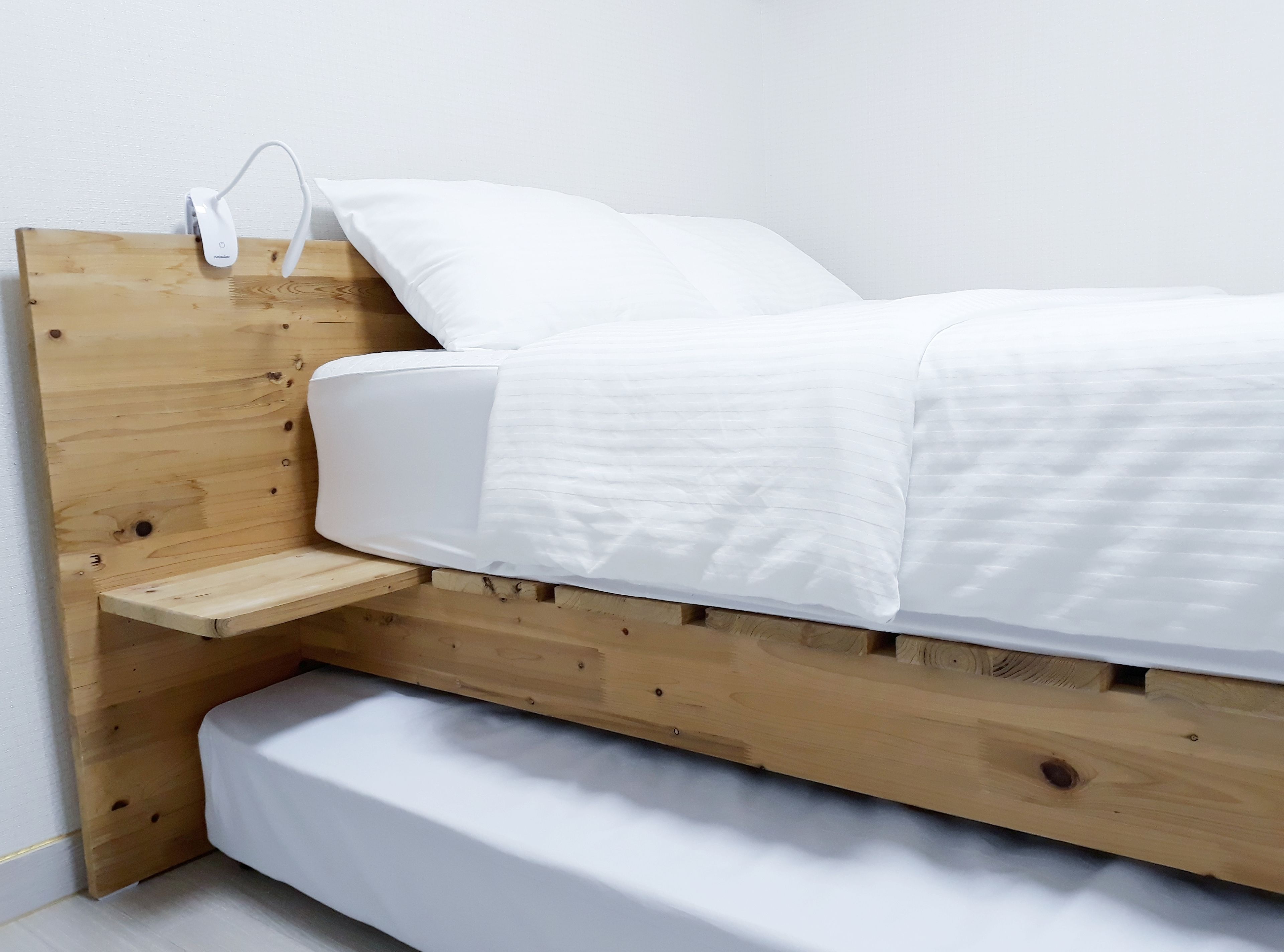 Ein hölzernes Bett mit weißer Matratze und Kissen, ein Nachttisch und eine wandmontierte Ladestation.