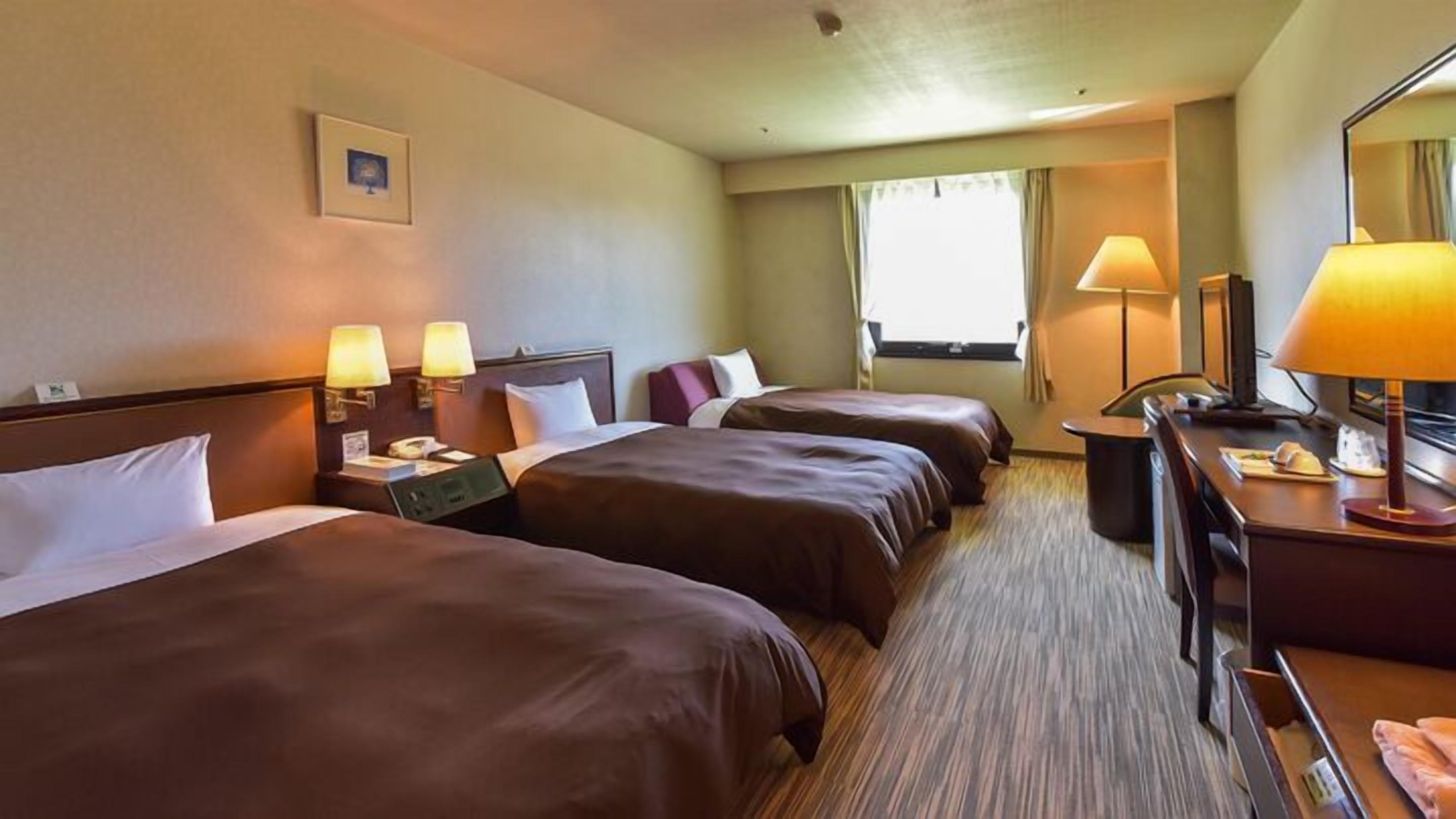 A hotel room with two beds, a desk, a chair, a lamp, and a window.