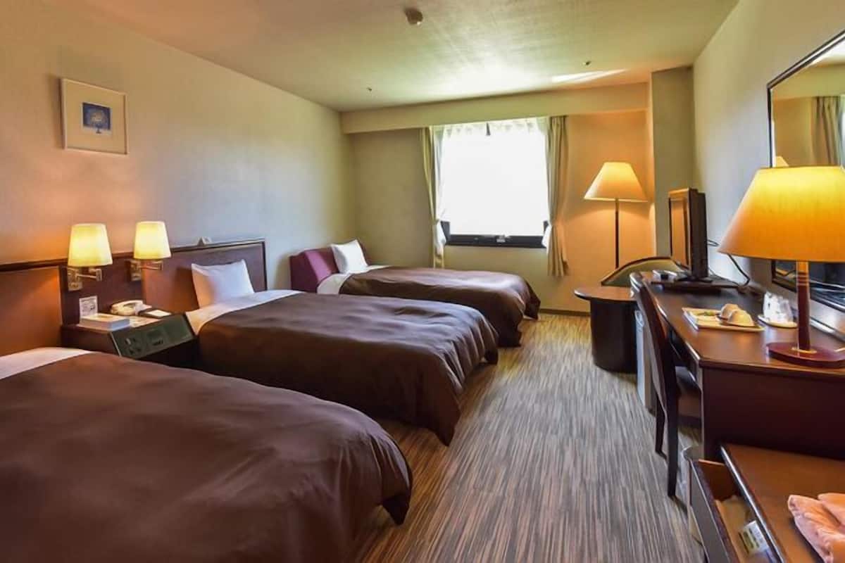 Une chambre d’hôtel avec deux lits, un bureau, une chaise, une lampe et une fenêtre.