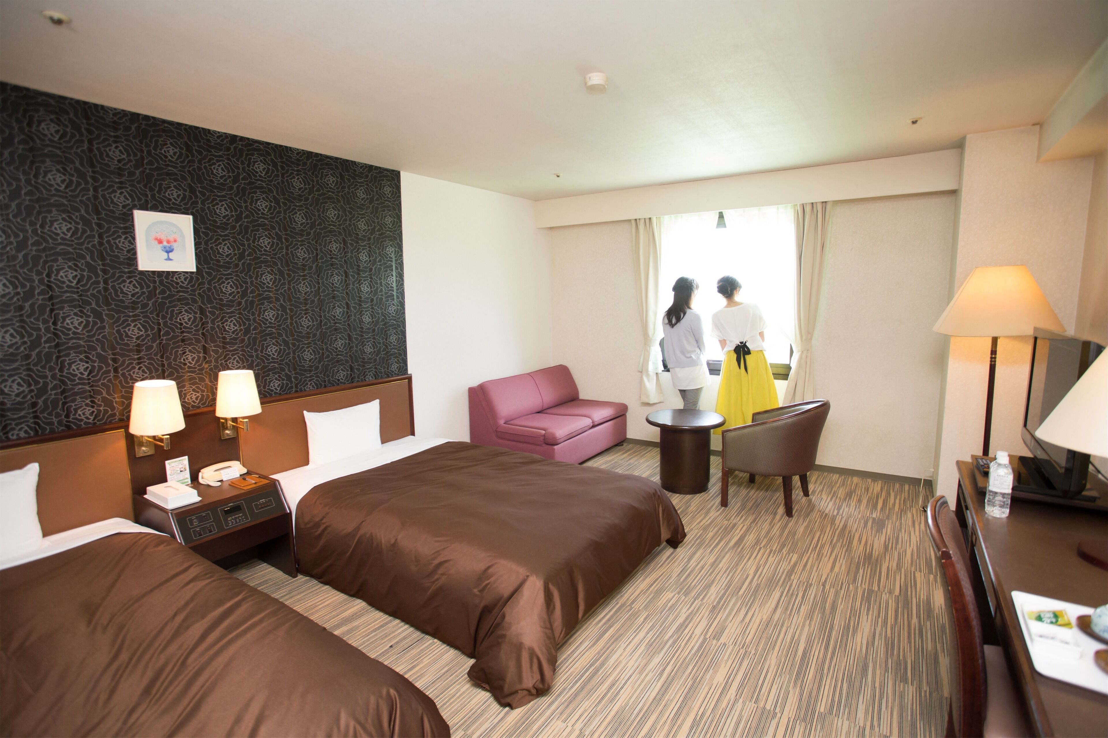 Une chambre d’hôtel avec deux lits, un bureau, une chaise, une petite table et une vue sur l’extérieur.