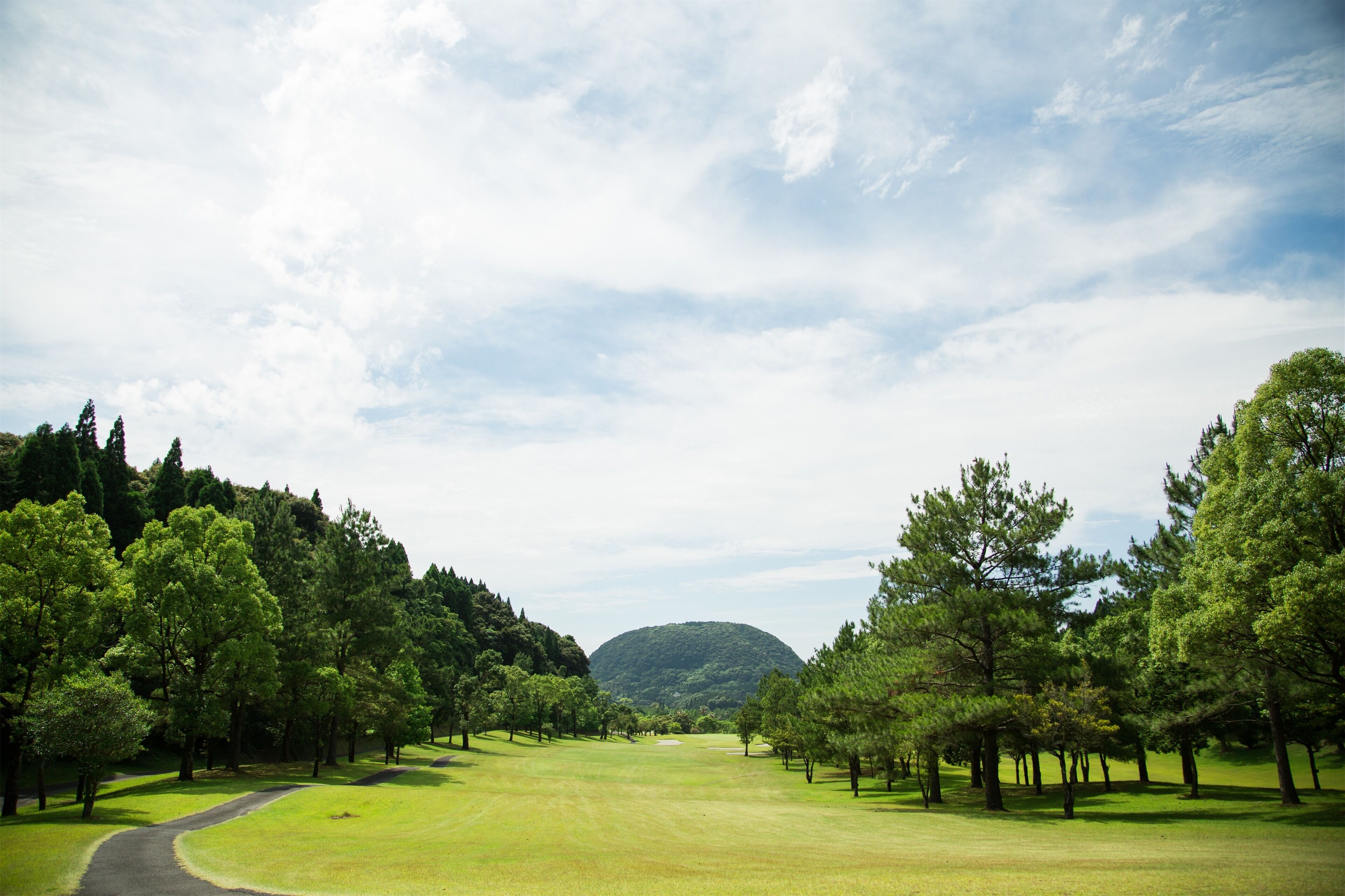 A golf course with a path leading to a distant hill.