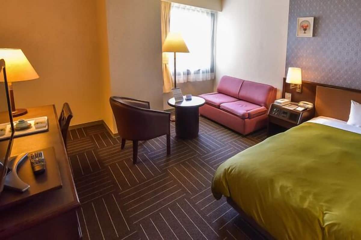 Une chambre d’hôtel avec un lit, un bureau doté d’une lampe, une chaise, une petite table et un canapé rose.