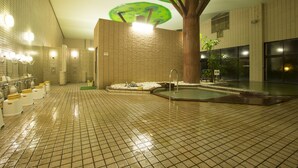 Een ruim overdekt zwembad met betegelde vloer, een centraal waterornament en een constructie die op een boom lijkt, met groene parasols.