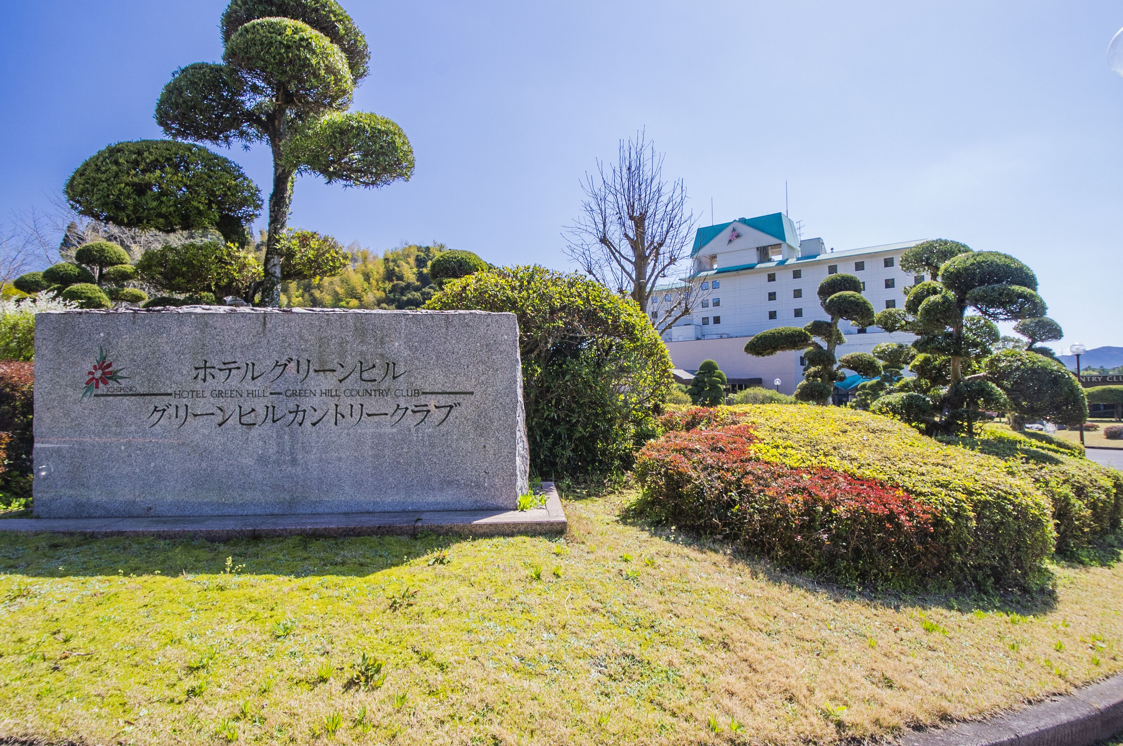 A stone sign with Japanese text, surrounded by well-maintained bushes and trees.