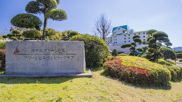A stone sign with Japanese text, surrounded by well-maintained bushes and trees.