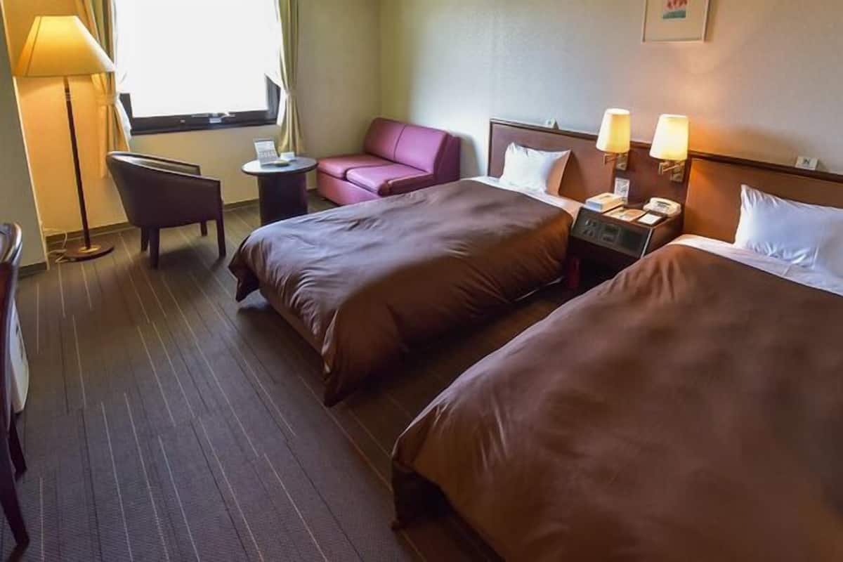 Une chambre d’hôtel avec deux lits, un bureau, une chaise, une lampe et une fenêtre.