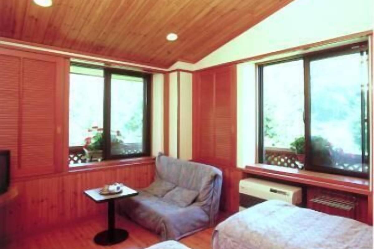 Une pièce chaleureuse avec des boiseries, un canapé, une petite table et de grandes fenêtres donnant sur un paysage verdoyant.