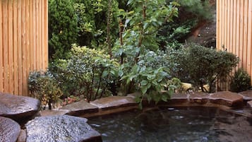 A wooden deck with a small pond, surrounded by lush greenery and a wooden fence.