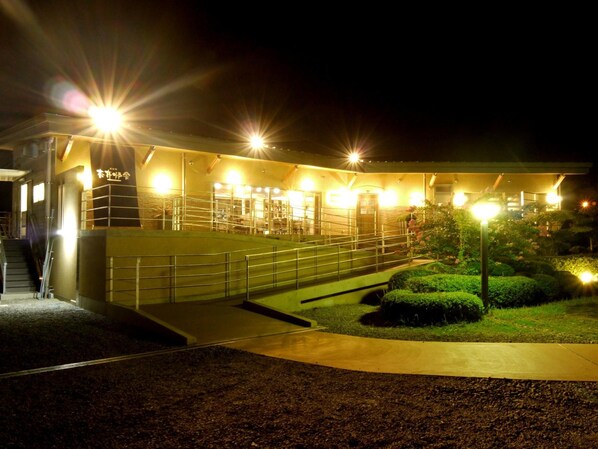 A building with a ramp leading to a covered area, surrounded by a landscaped garden with bushes and a pathway. - Matsushima Kanko Hotel MISAKITEI (Kamiamakusa)