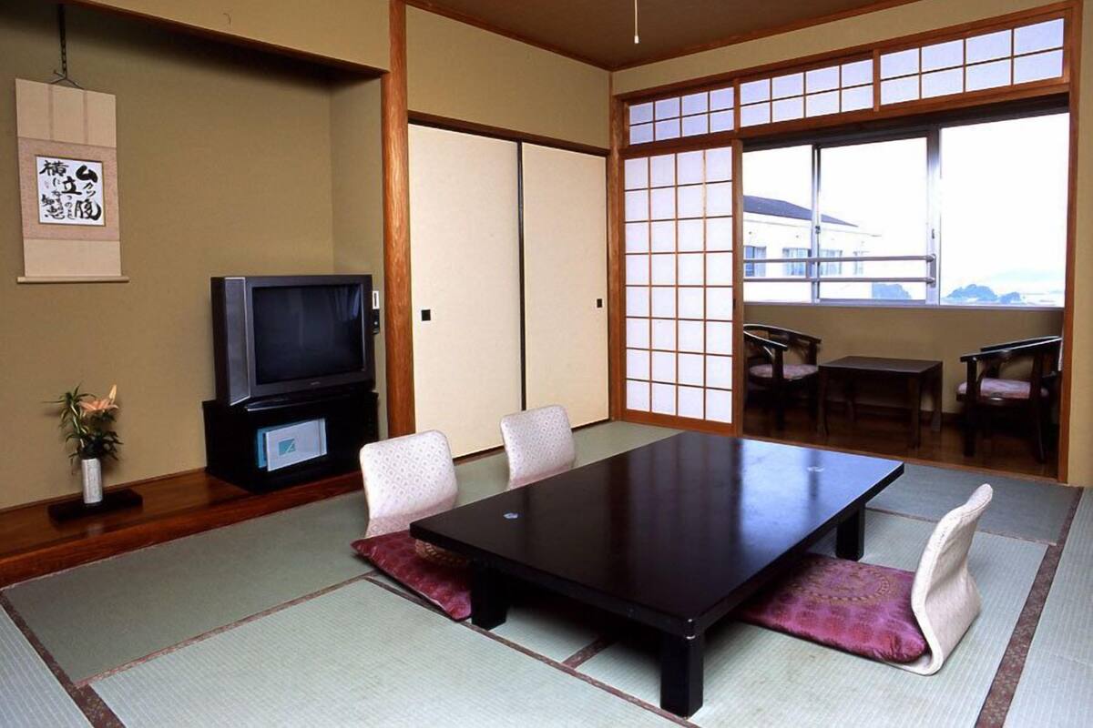 A traditional Japanese room with tatami flooring, a low table, chairs, a television, and a sliding door with shoji screens.