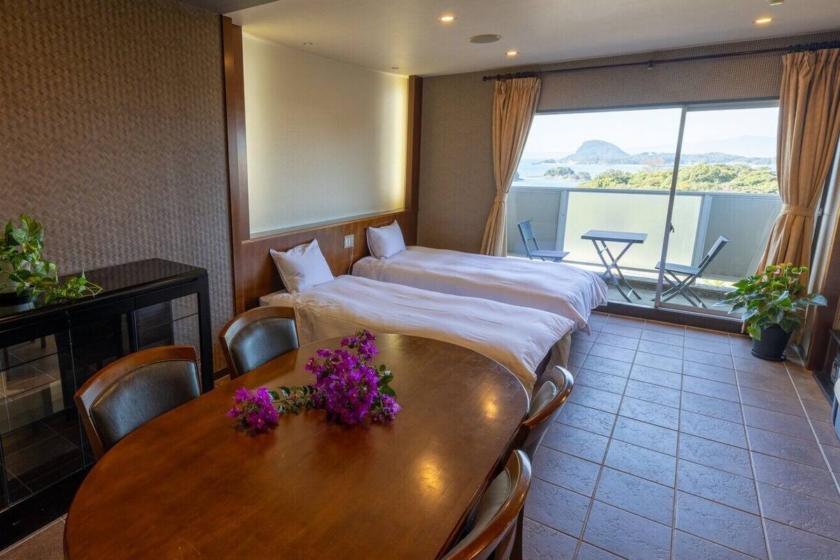 A hotel room with a balcony, a dining table with chairs, and a bed with white bedding.