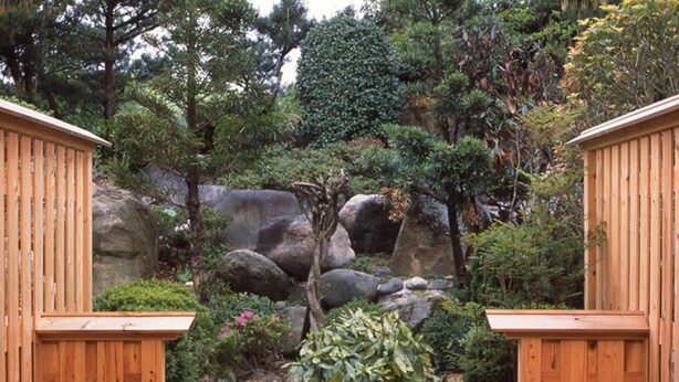 Un baño de aguas termales de madera rodeado de rocas y vegetación.