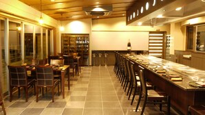 Una larga mesa de comedor con sillas, una alacena para vinos y una zona de bar en una habitación bien iluminada con suelo de baldosas.