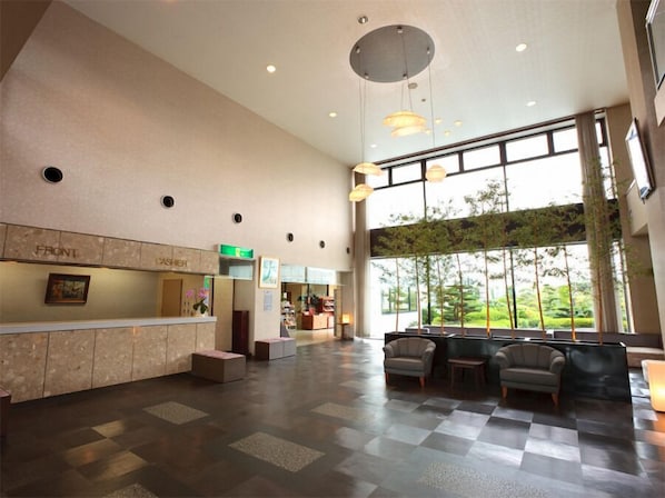 A spacious lobby with a reception desk, seating area, and large windows offering a view of greenery.