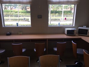 A room with a long table, several chairs, two windows with views of greenery, and a microwave on the table. - Idaimae Green Hotel (Saga)