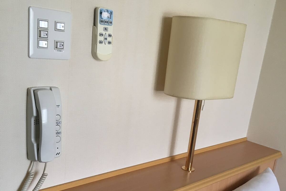 A hotel room with a bedside telephone, a control panel, a lamp, and a pillow.