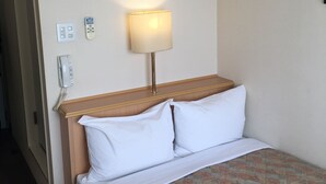 Habitación de hotel con cama, lámpara de noche, aire acondicionado, teléfono y toma de corriente.