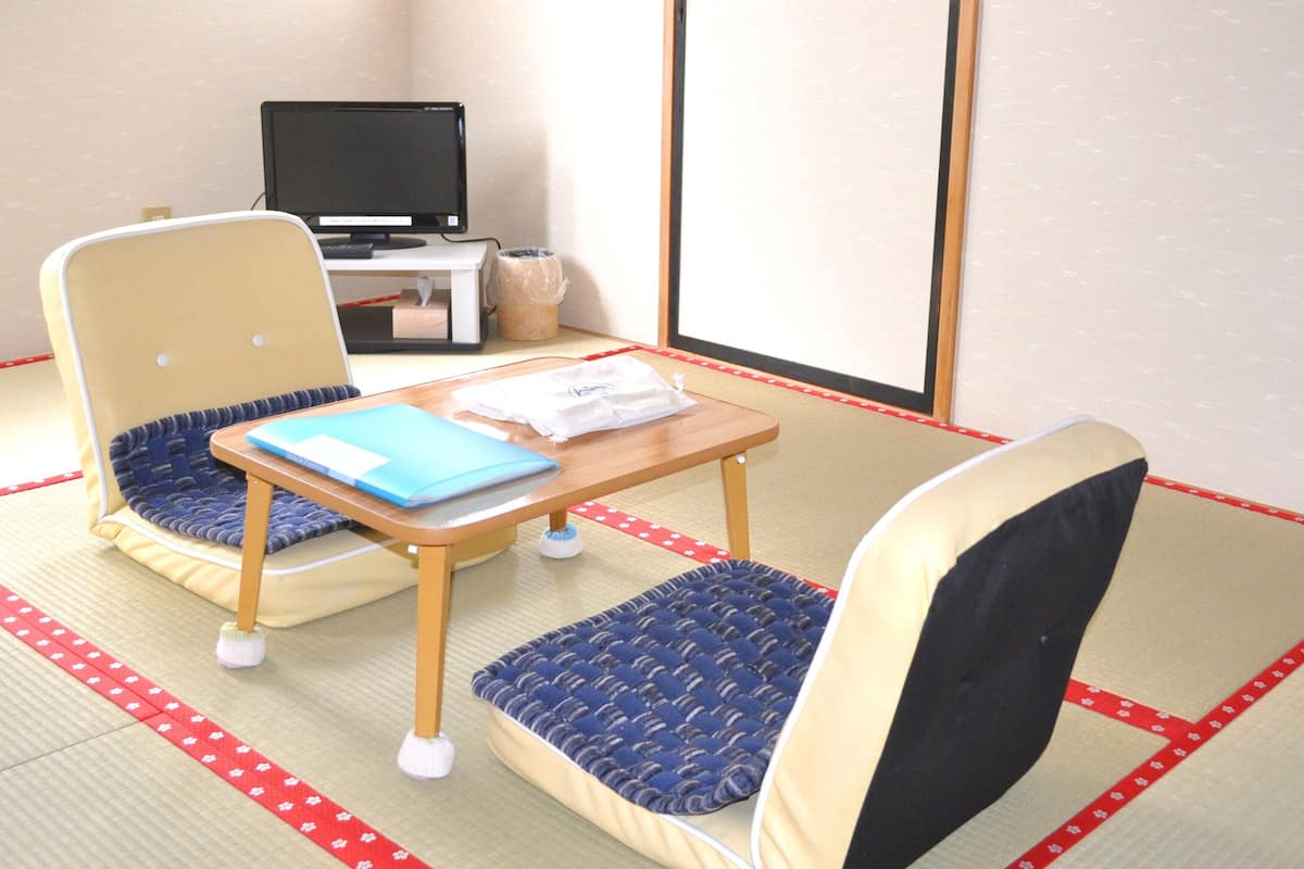Ein Raum mit Tatami-Matten, bestehend aus zwei Tatami-Matten, einem Holztisch, zwei Tatami-Stühlen, einem Laptop und einer kleinen Mülleimer.