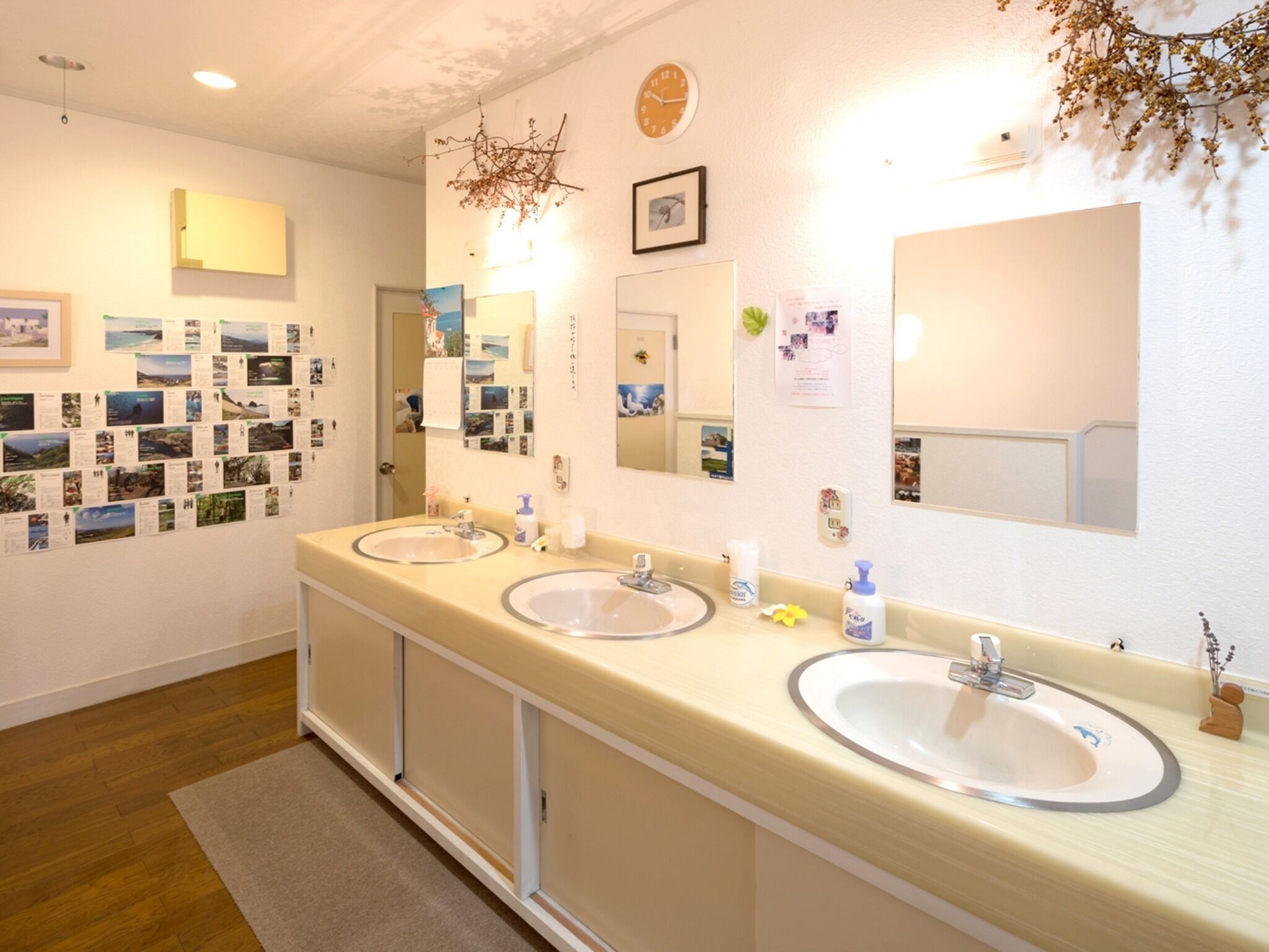 A hotel bathroom with two sinks, a mirror, a clock, and a wall decorated with photos.