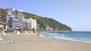 Una playa con edificios en una ladera, cielo despejado y mar tranquilo.
