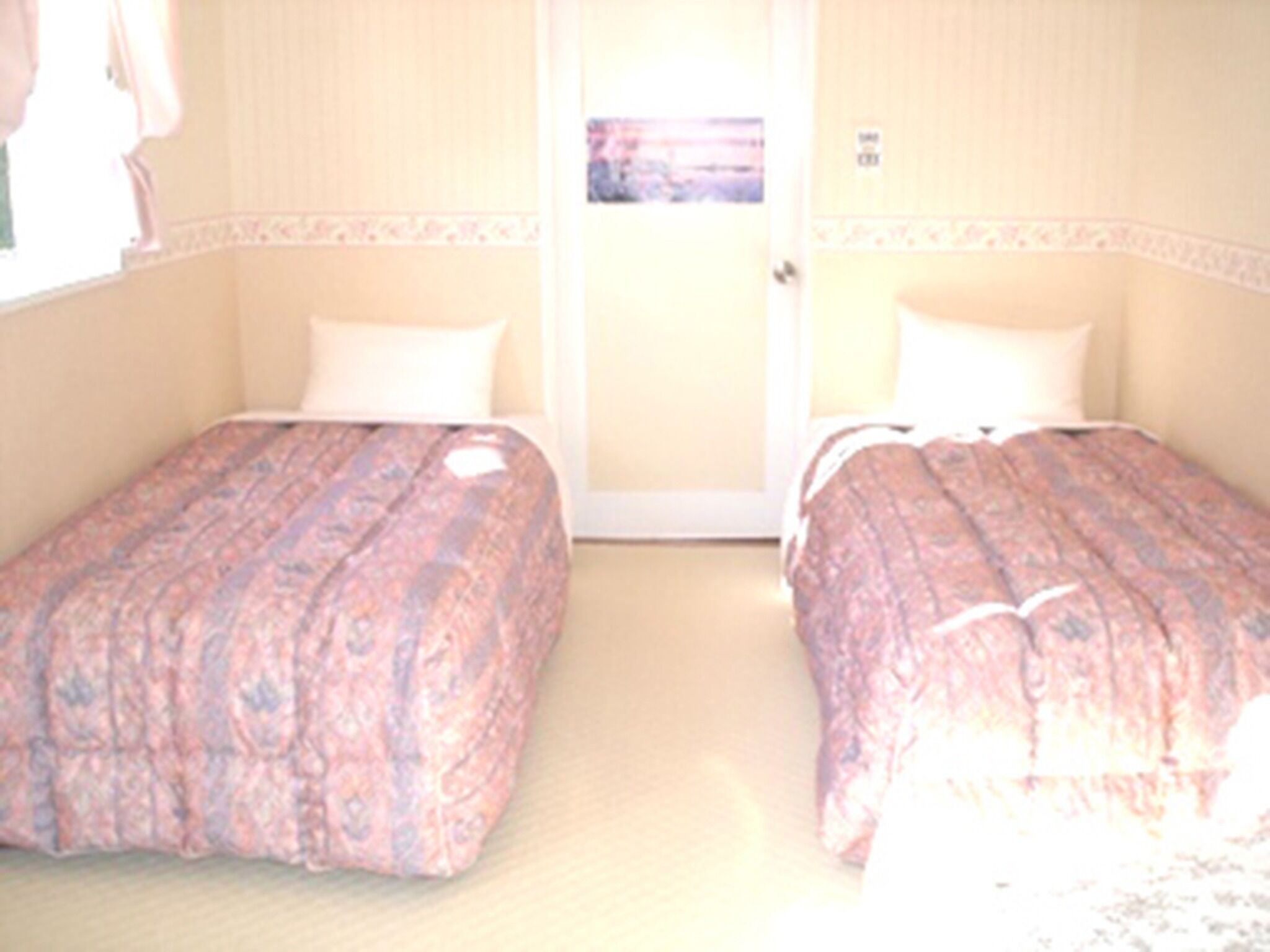 A hotel room with two beds, a door, and a window.