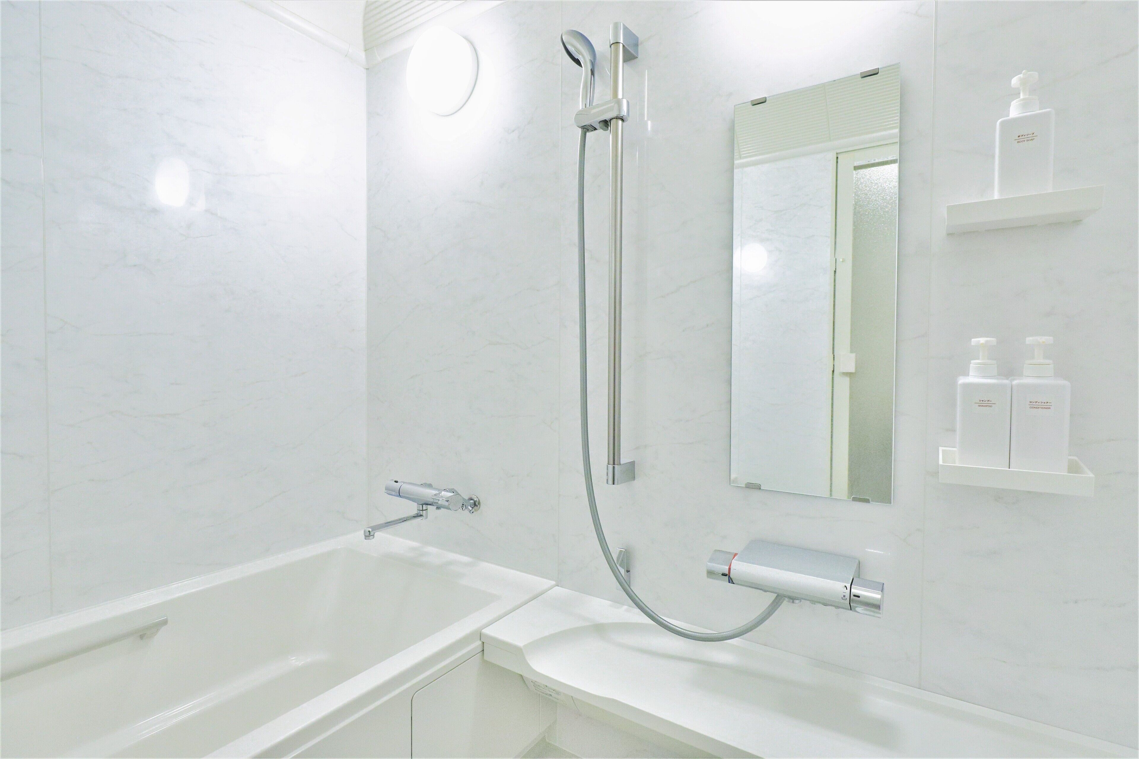 Et moderne badeværelse med badekar, bruser med håndbruser, toiletpapirholder og et spejl.
