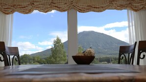 A dining table with a bowl of food, two chairs, and a view of a mountain through large windows with curtains. - BLISS Villa TSUBAKI (Kutchan)