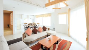 A spacious living area with a sofa, a coffee table, and a dining area in the background. - BLISS Villa TSUBAKI (Kutchan)