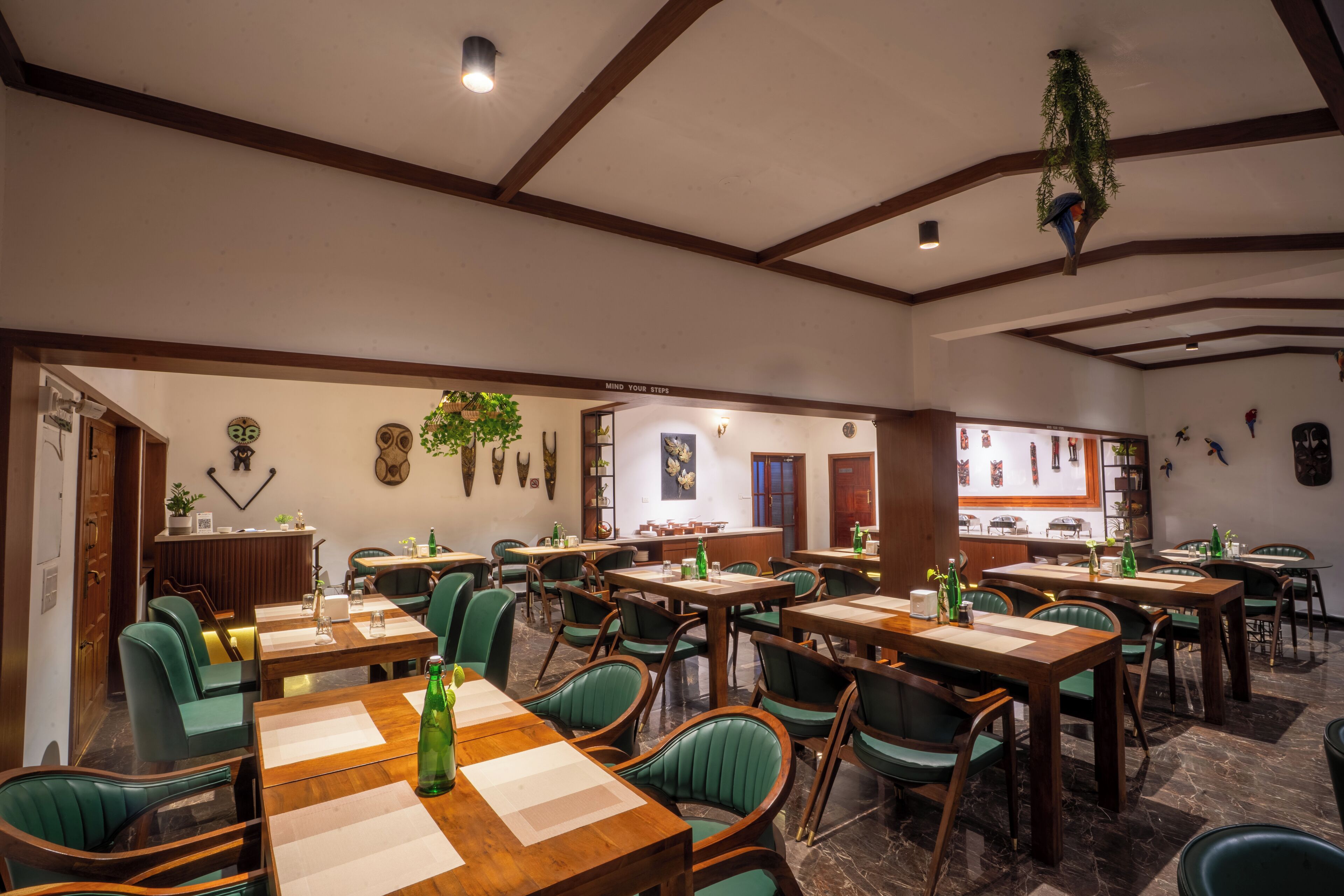 Un restaurante con mesas de madera y sillas verdes, una zona de bar y decoración en las paredes.