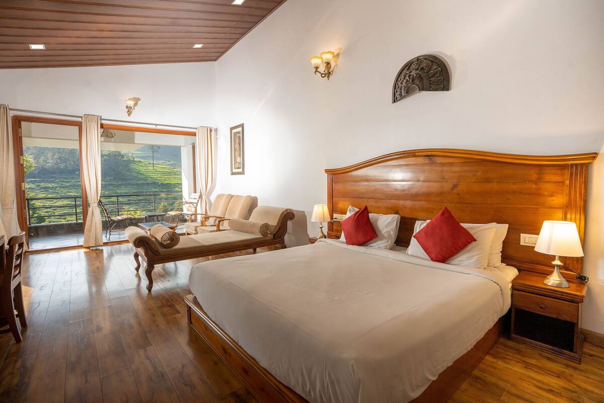 Ein geräumiges Schlafzimmer mit einem großen Bett, einem Holzkopfende und einem Nachttisch mit Lampe. Ein Balkon bietet Blick auf Grünflächen.