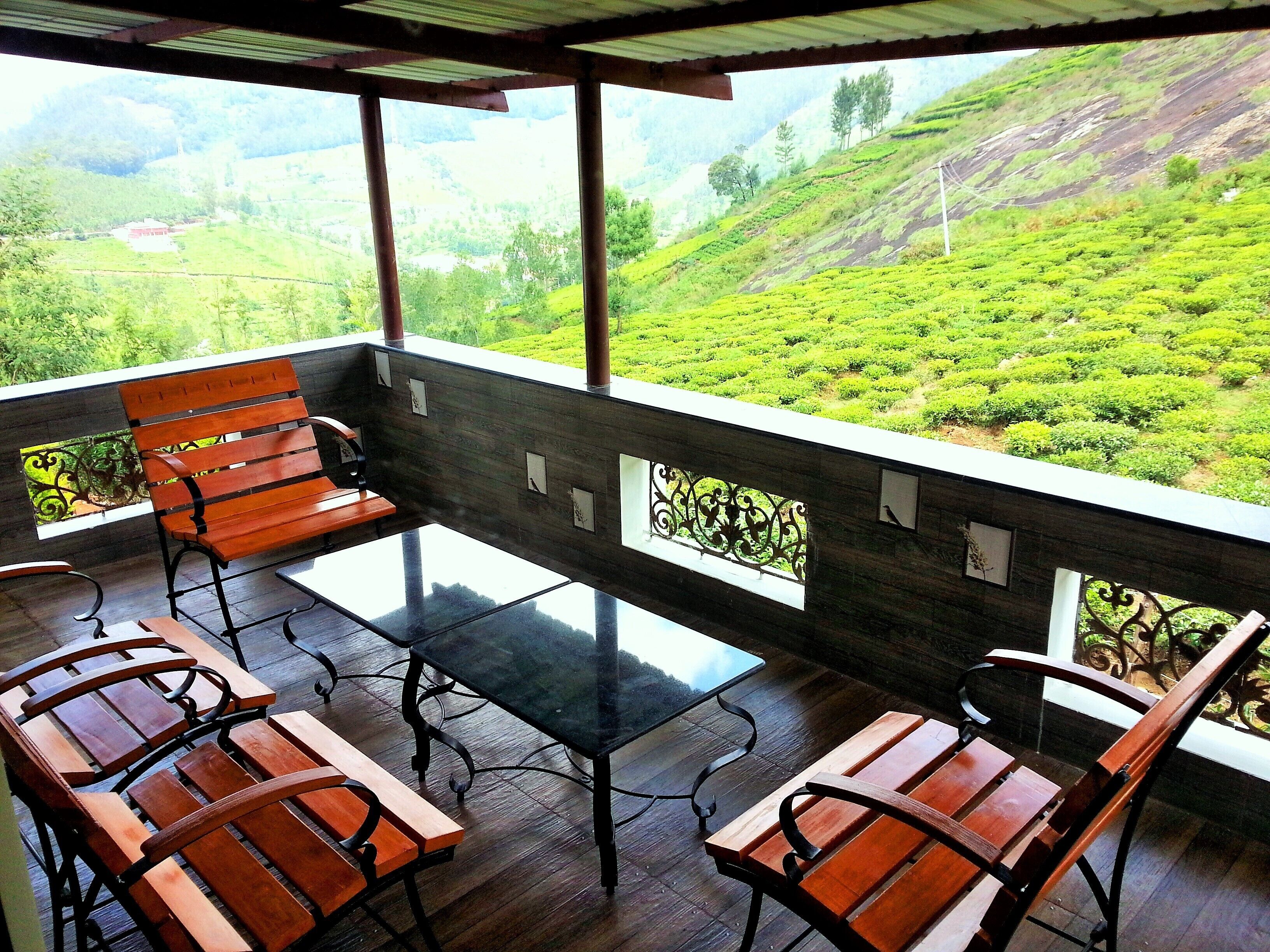 A terrace with wooden furniture and a glass table, overlooking a lush green landscape.