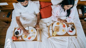 A couple in bed with breakfast trays.