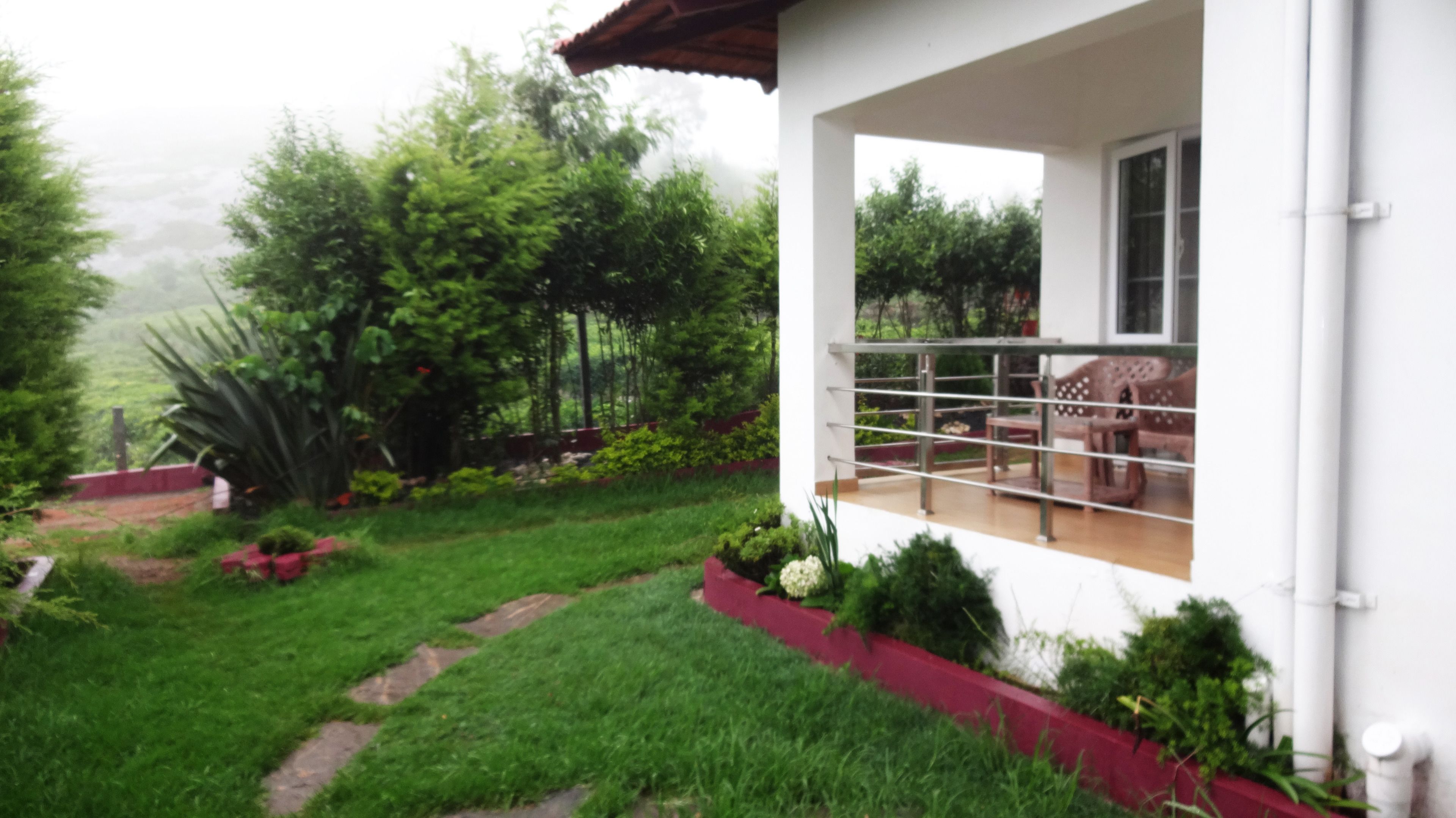 A white house with a balcony, surrounded by a garden with various plants and a red border.