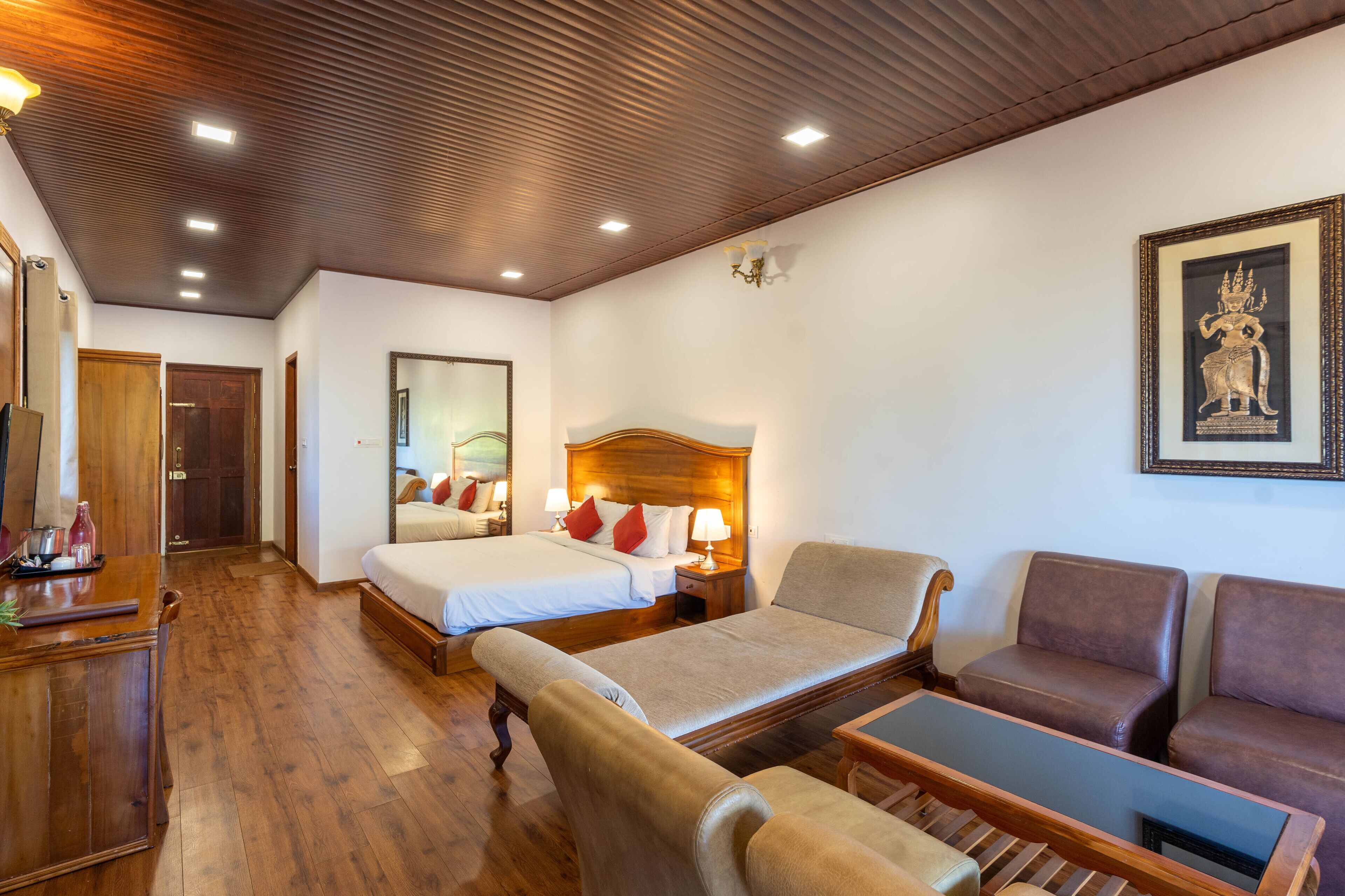 Une chambre d’hôtel avec un plafond en bois, un lit avec une literie blanche, un canapé, une petite table et un tableau encadré au mur.