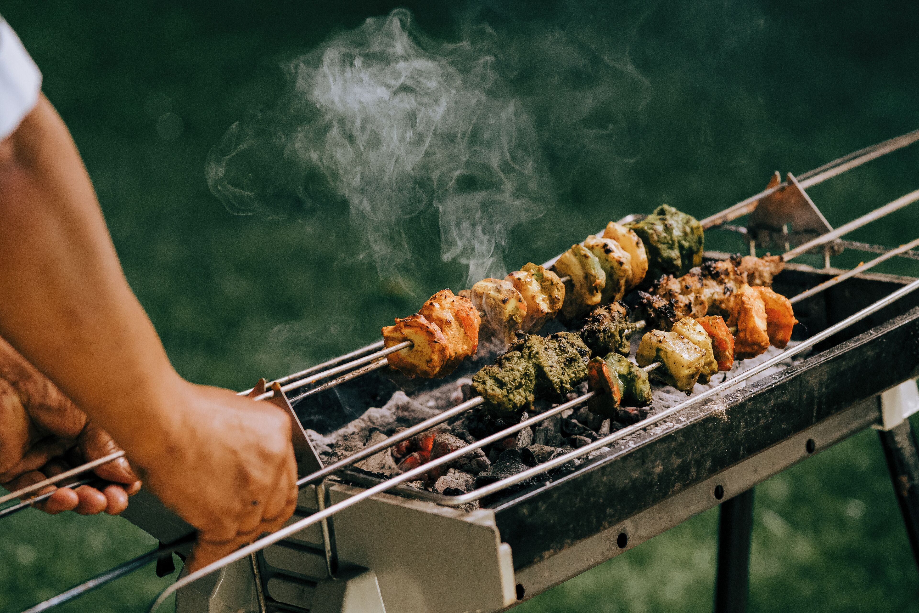 Una persona preparando carnes y verduras a la parrilla.