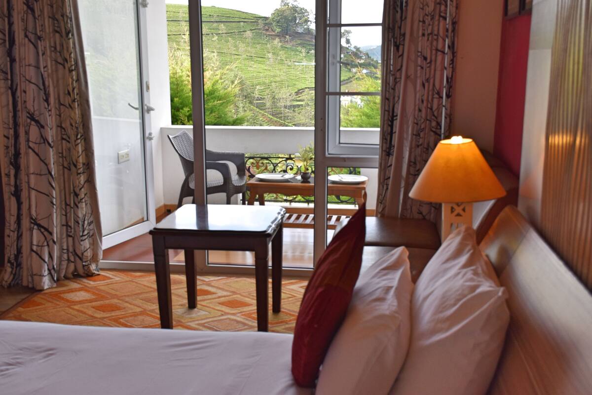 Ein Hotelzimmer mit Bett, Tisch und Stuhl. Durch das Fenster ist eine grüne Landschaft zu sehen.