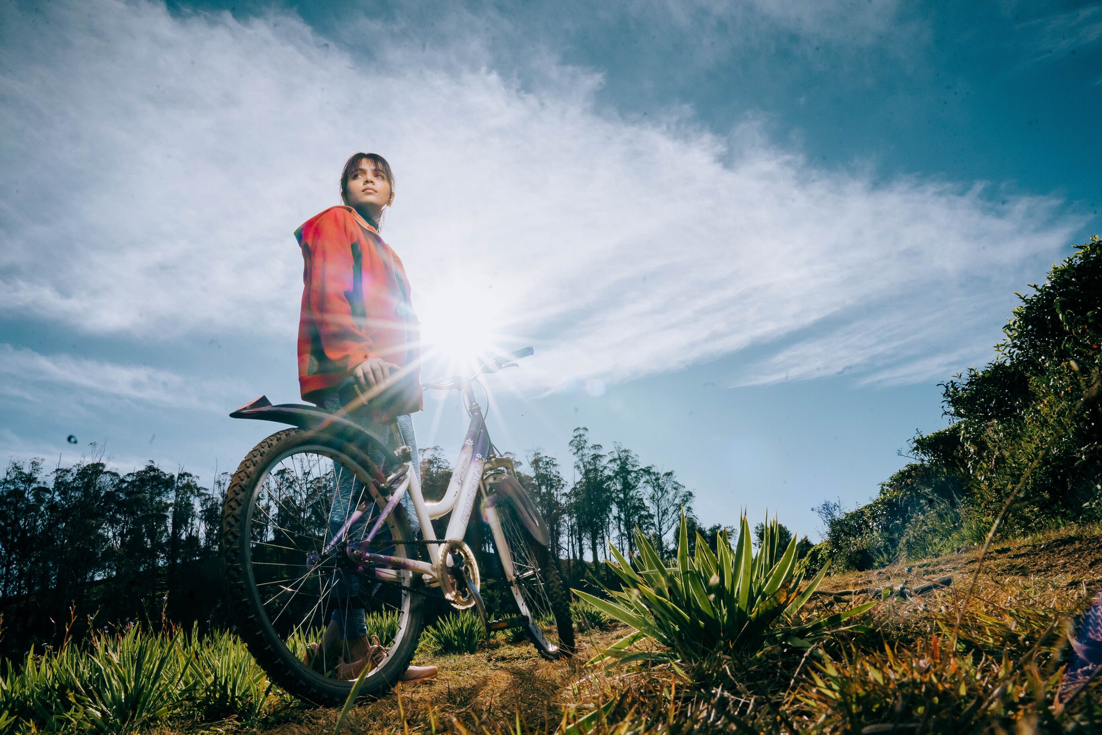 A person standing next to a bicycle on a grassy hill with trees in the background.