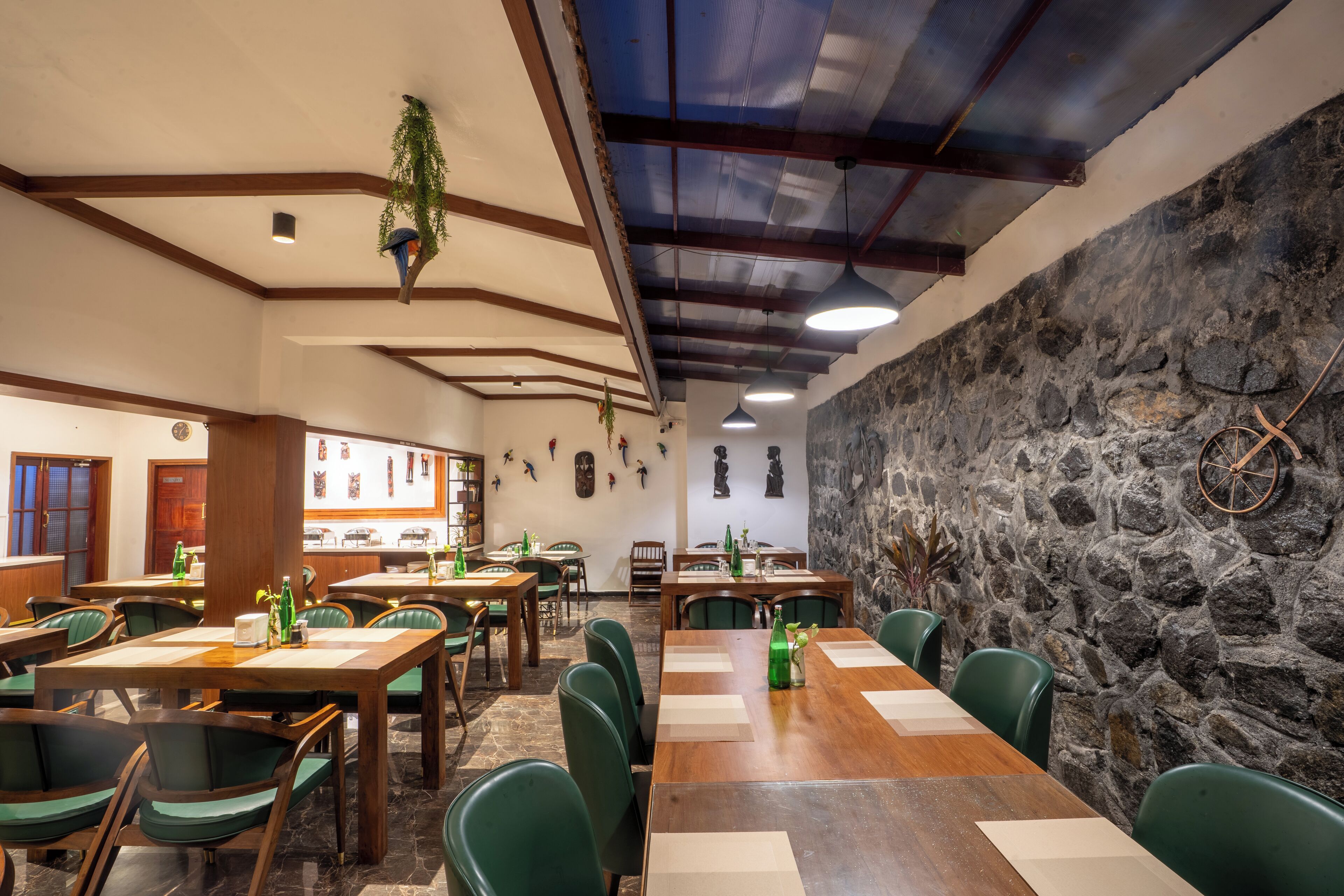 A restaurant with wooden tables and green chairs, stone walls, and hanging plants.