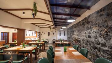 A restaurant with wooden tables and green chairs, stone walls, and hanging plants.