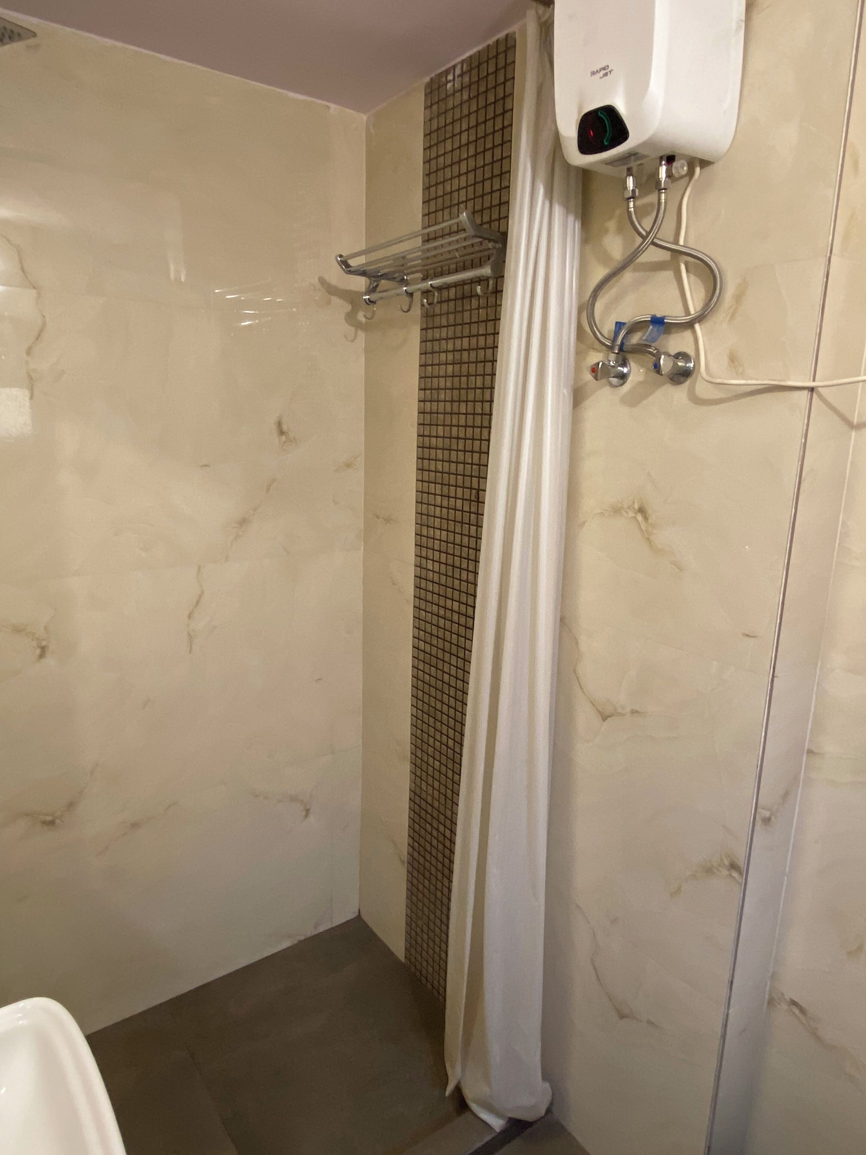 A bathroom with a shower, a towel rack, and a hand dryer.