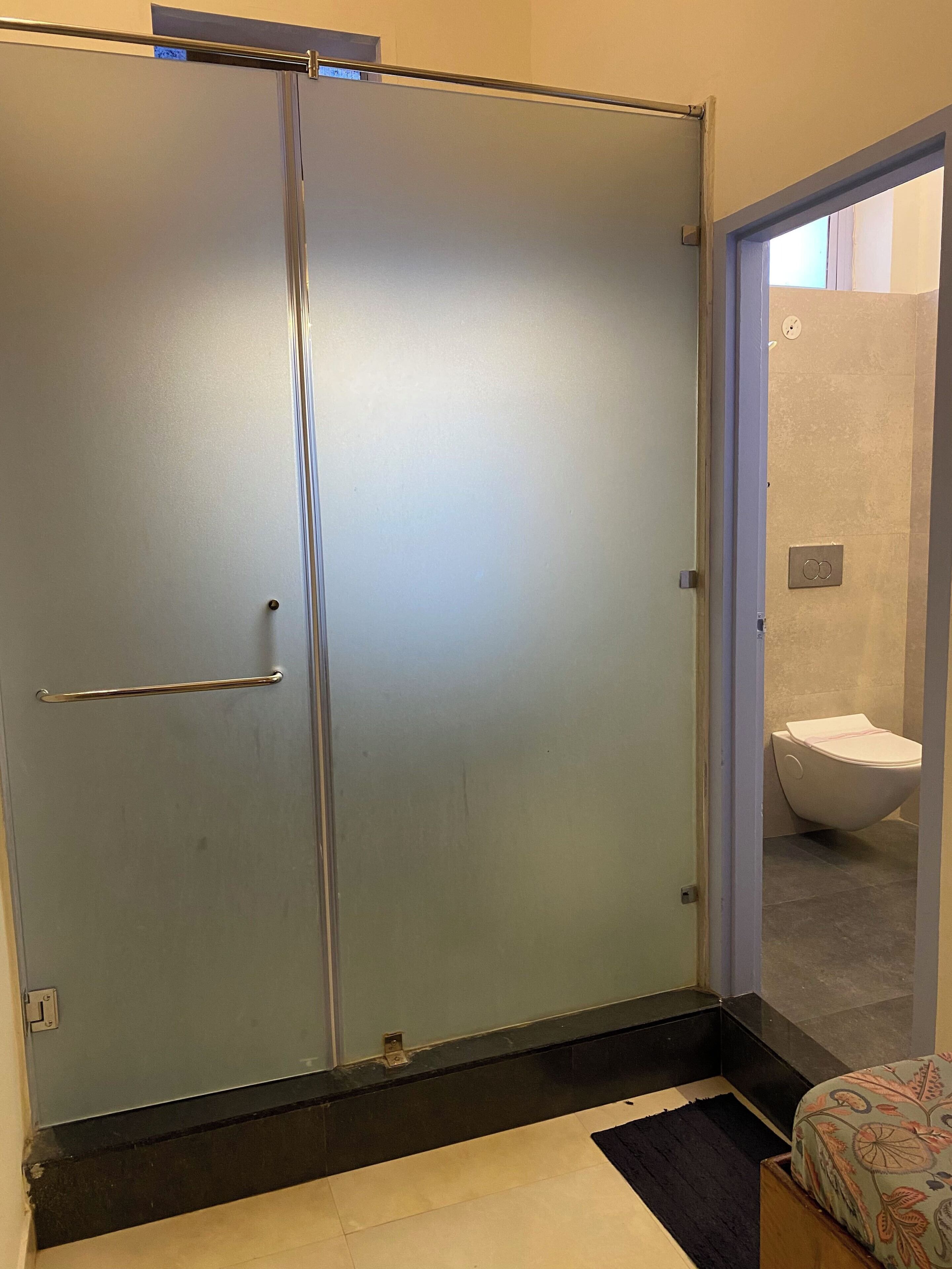 Un baño con inodoro, ducha y una puerta de vidrio que da a un pasillo.