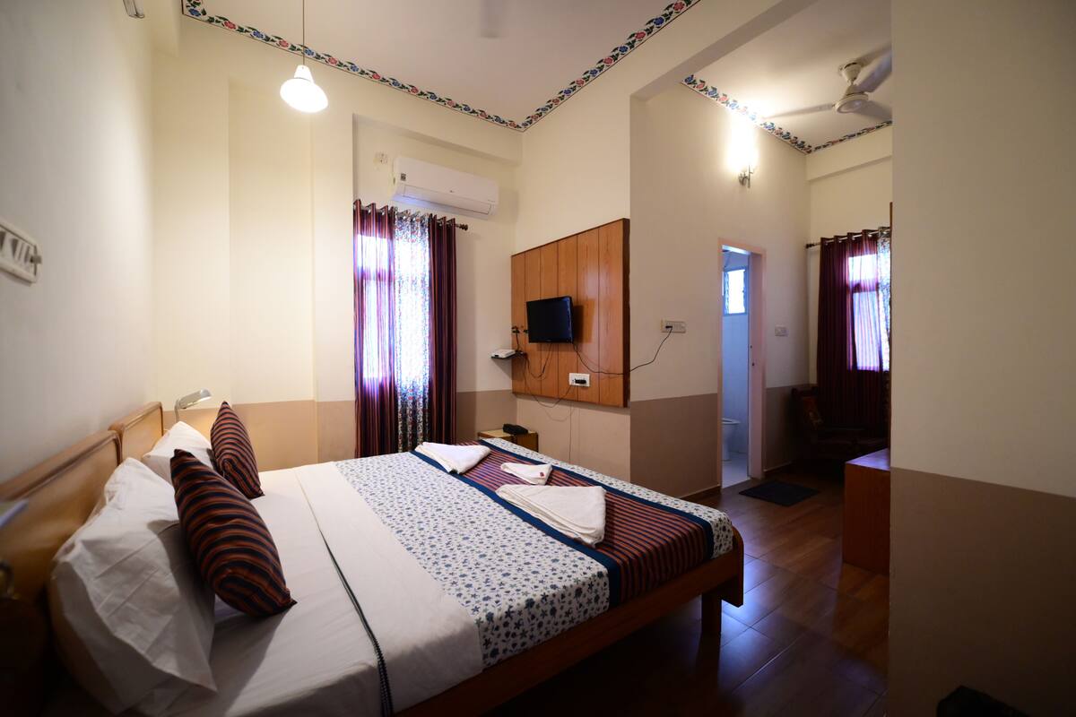 Una habitación de hotel con una cama, un televisor montado en la pared y un ventilador de techo.