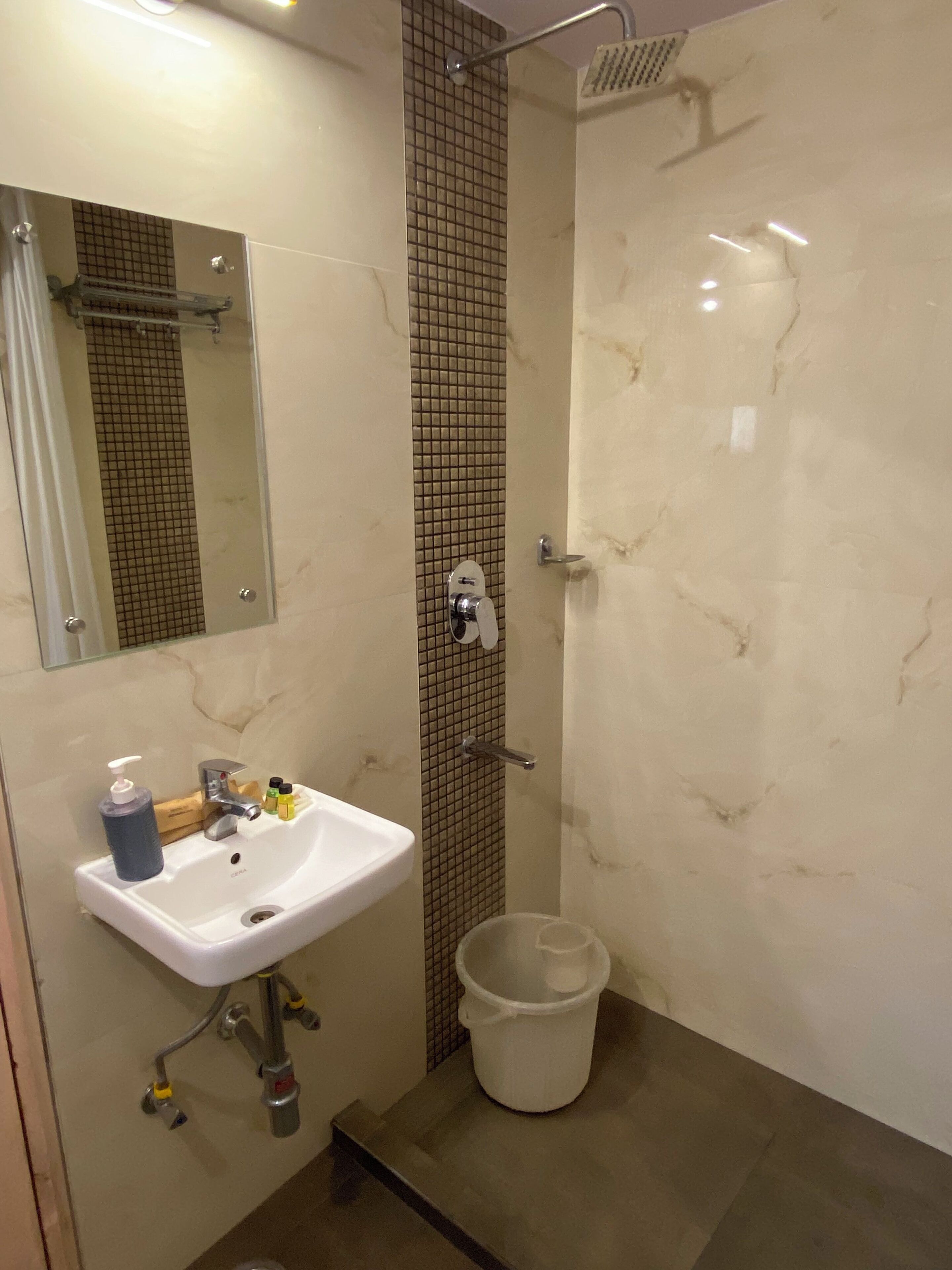 A bathroom with a white sink, a mirror, a shower, and a white bucket.