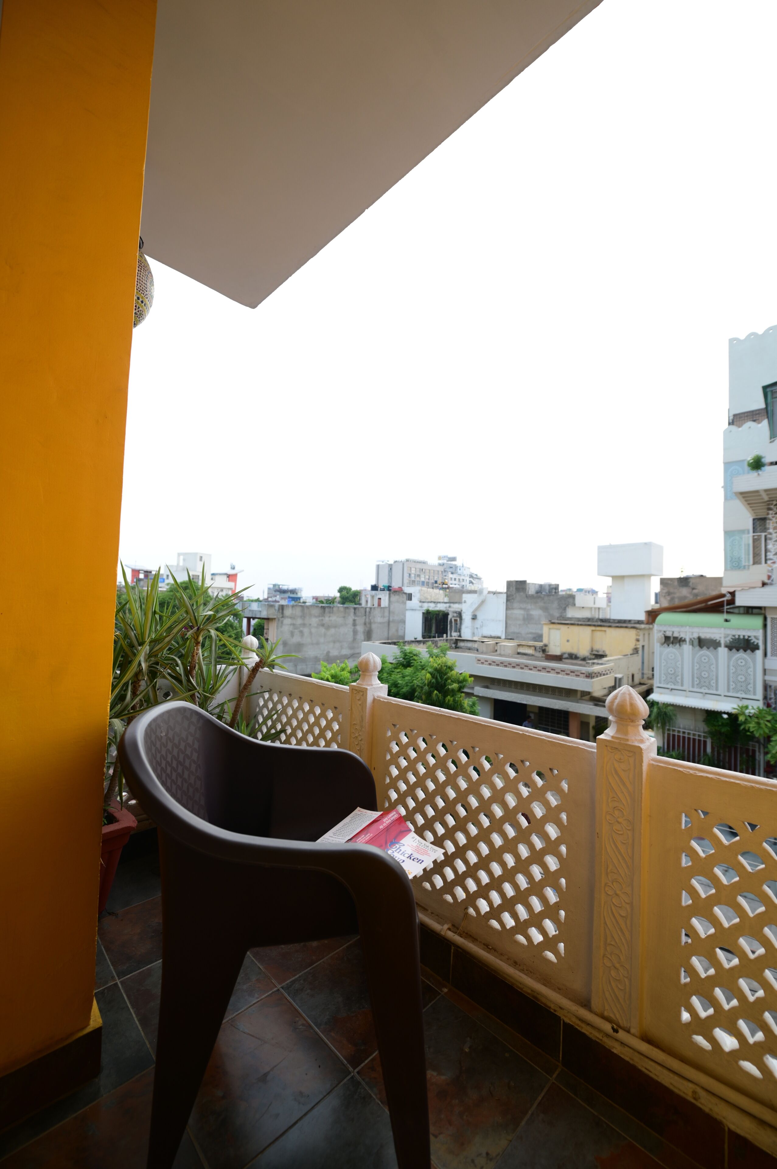 Ein Balkon mit Stuhl und Topfpflanze, mit Blick auf eine Stadtlandschaft mit Gebäuden.