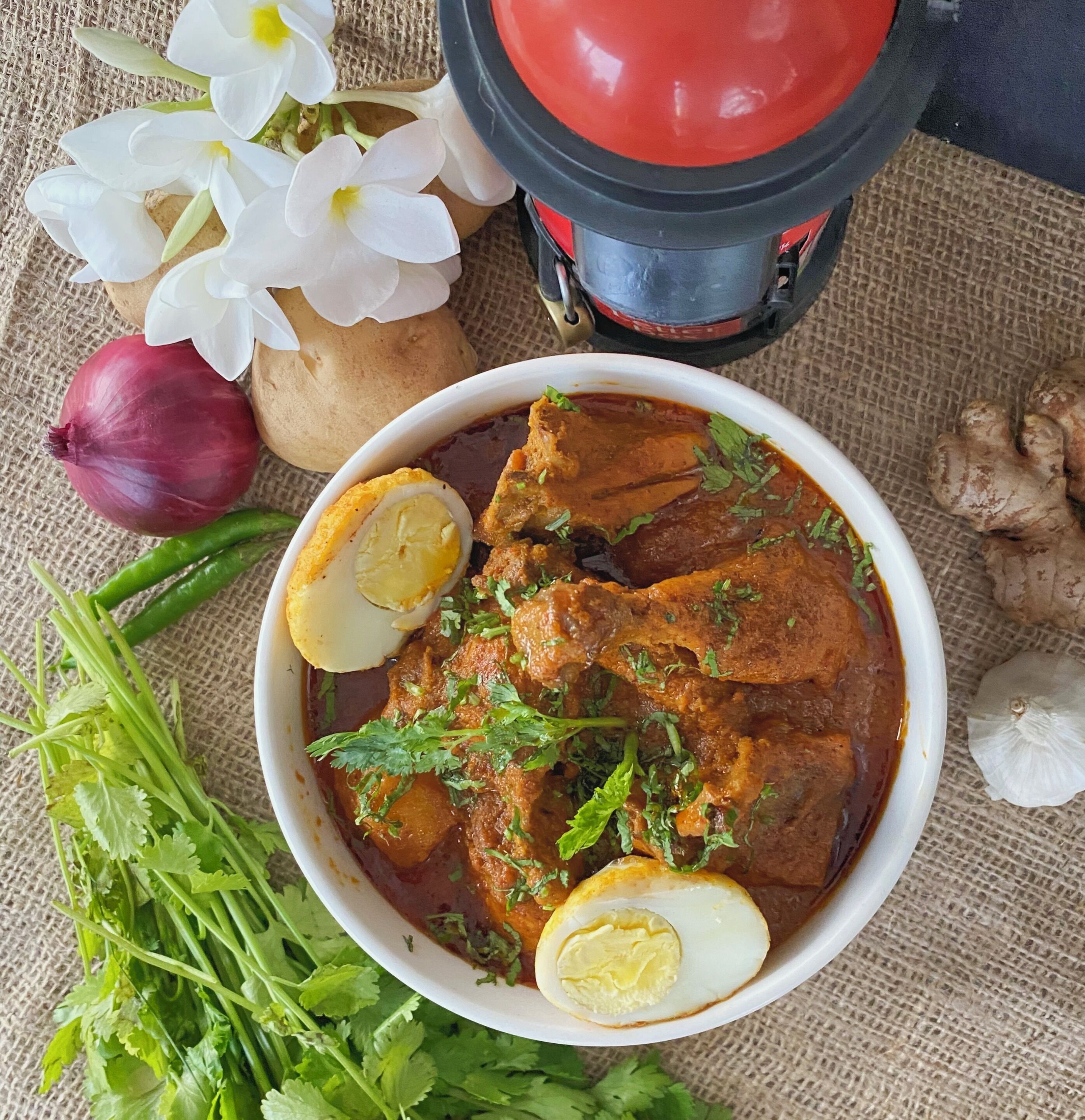 Eine Schüssel mit Curry, gekochten Eiern und frischen Kräutern, umgeben von Gemüse und einem roten Behälter.