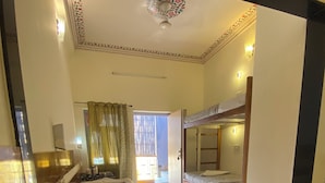 A bedroom with a bunk bed, a bedside table, a window with curtains, and a ceiling fan. - Chitra Katha - A Story Per Stay (Jaipur)